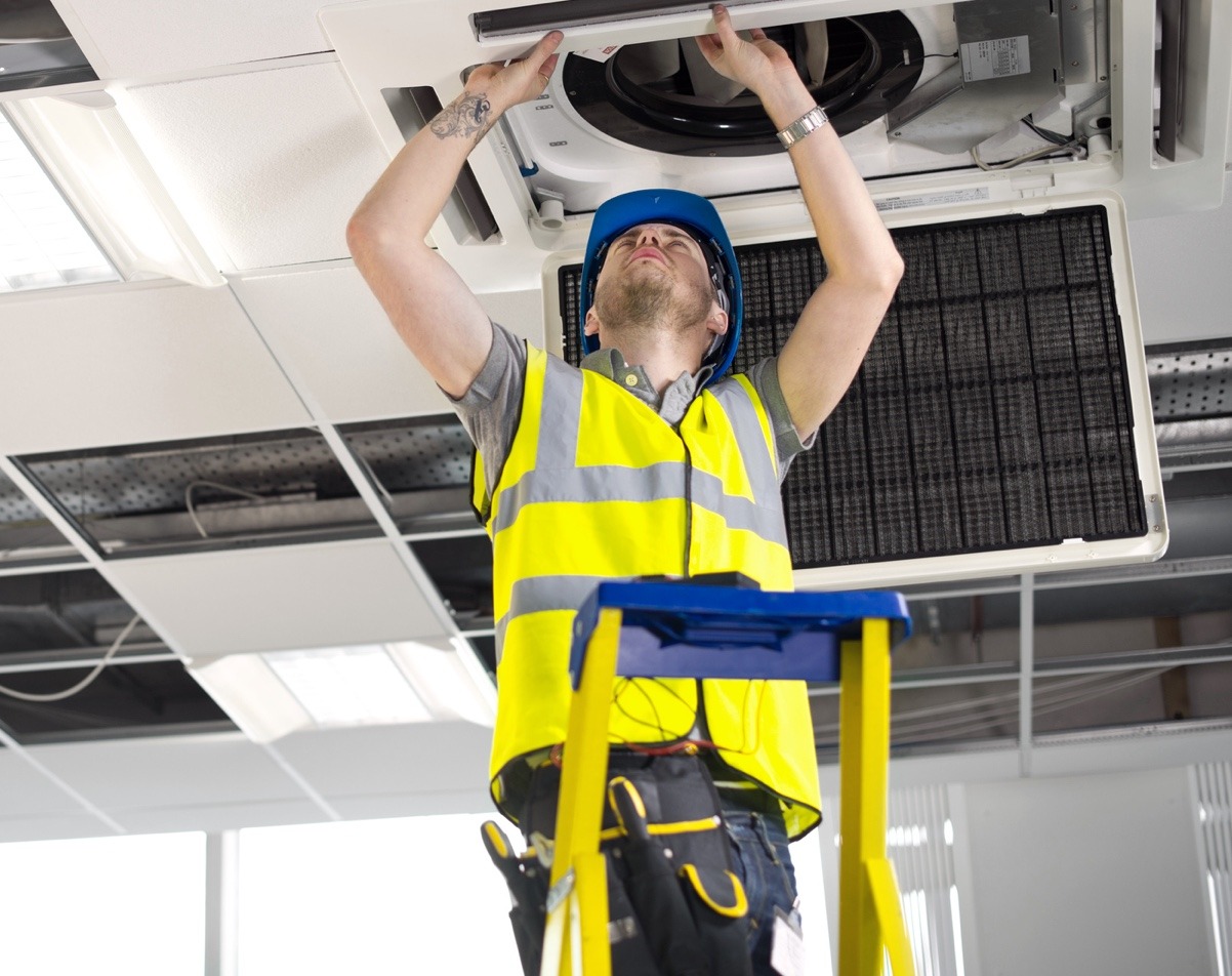 HVAC service technician installing ceiling ventilation for a commercial heating and cooling system 